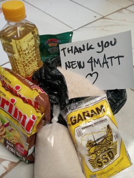 A photo of grocery items including a bottle of oil, Maggi seasoning cubes, rice, and sugar, with a handwritten note reading "THANK YOU NEW GMATT" with a heart.