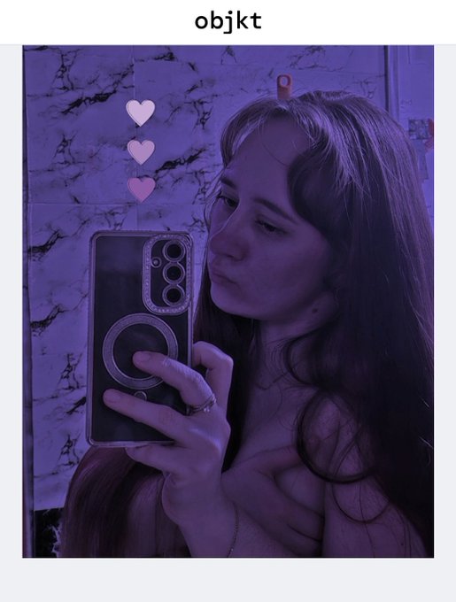 A person with long hair takes a purple-tinted mirror selfie holding a phone with a large circular camera cover, with the text "objkt" displayed at the top.