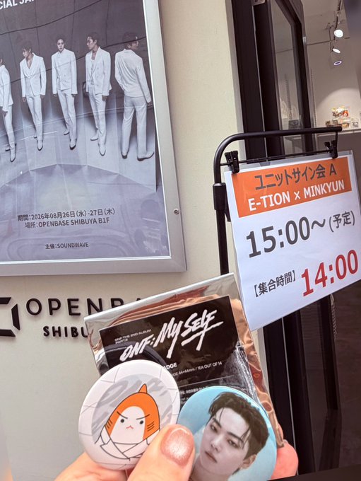A fan holds up "ONE In My Self" merchandise featuring E-TION's photo next to a posted sign for the E-TION x MINKYUN unit signing event at OPENBASE SHIBUYA on August 26-27, with a 14:00 gathering time and 15:00 signing — capturing the excitement as fans wait to meet E-TION.