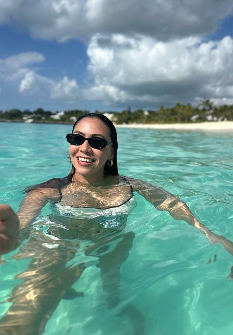 A smiling woman wearing sunglasses in clear turquoise tropical waters at a beach destination.