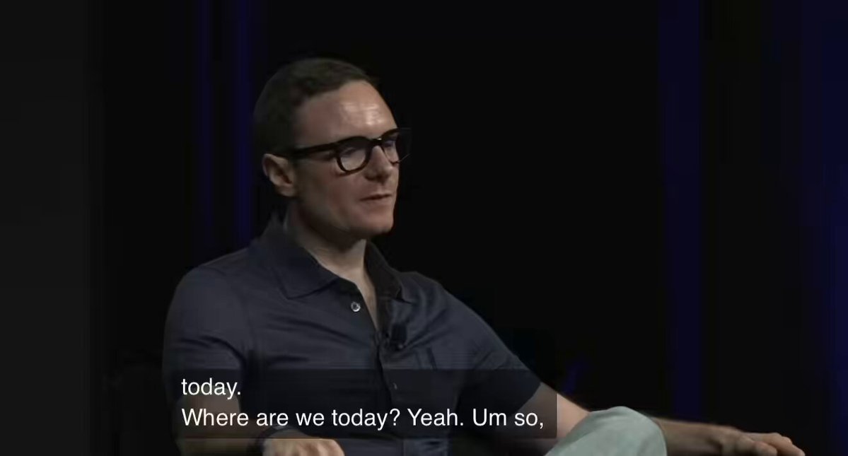 The image shows a man wearing glasses sitting down, possibly talking or giving a speech at an event. The text above him reads "Today, Where are we today? Yes, um, I'm so." This suggests that he might be discussing the current situation or sharing his thoughts on the topic of discussion.
