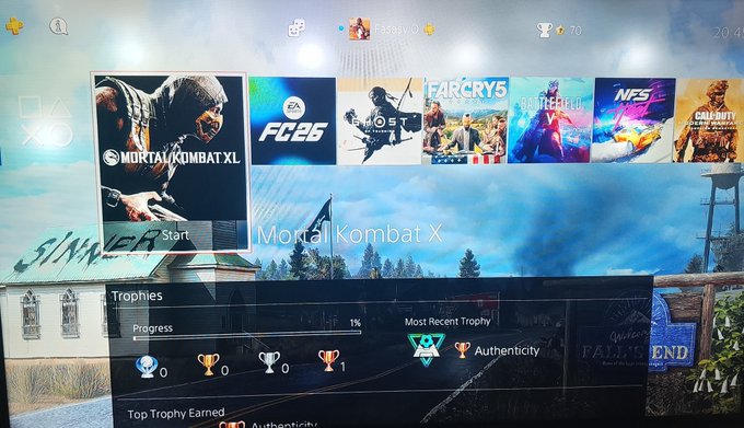 A PlayStation trophy list screen showing various game tiles including Mortal Kombat XL, FC 25, Ghost of Tsushima, Far Cry 5, Battlefield 2042, NFS, and Call of Duty, with Mortal Kombat X selected showing 1% progress and an 'Authenticity' trophy.