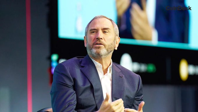 A photograph of Ripple CEO Brad Garlinghouse speaking on stage, with a 'CoinDesk' logo visible in the background.