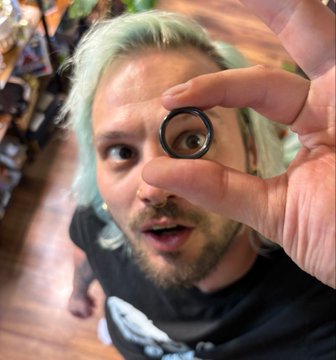 The image shows a man holding up a ring with one hand while looking at it through his other hand. The ring appears to have a black band and is made of metal. There are no texts or other objects visible in the image, so we can only see the ring and its details. Based on this information, it seems that someone has found an interesting object (the ring) and is sharing their discovery with others through a video. The post might be discussing the ring's design, materials used, or possibly even its value.
