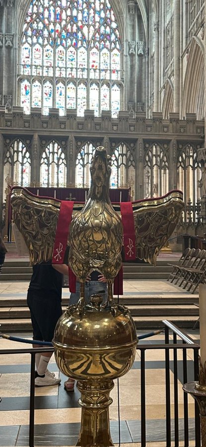 A golden eagle lectern with a red stole bearing Chi-Rho symbols stands inside a Gothic cathedral, beneath a towering stained-glass window — its outspread wings resembling the "X" in "XRP," visually echoing the post's equation of the cryptocurrency with "XP."