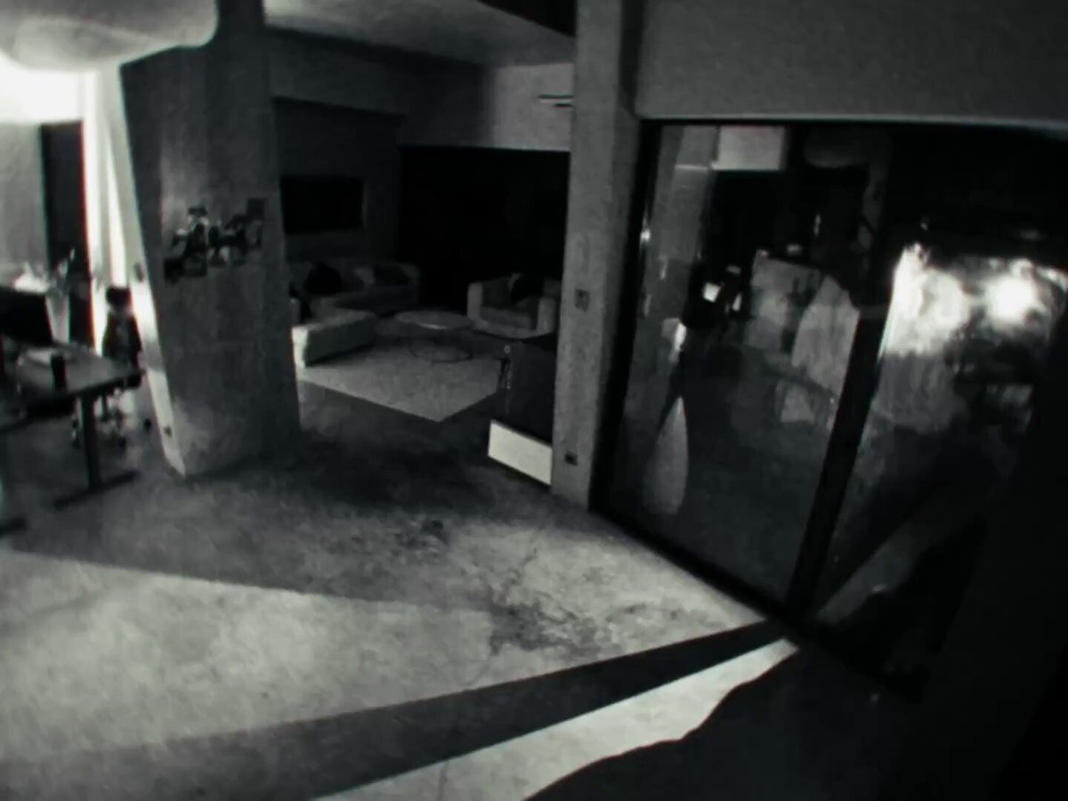 The image shows a room with a large window that reflects the outside world. The room appears to be empty, with no people present. There are two chairs placed near each other, one closer to the left side of the room and another on the right side. A couch is also visible in the background, located towards the center of the room. The scene seems to depict a staged event or a dramatic situation that has taken place within this space.