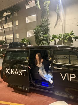 A young woman sits inside a black luxury van with its door open, labeled 'KAST' and 'VIP' in white lettering.