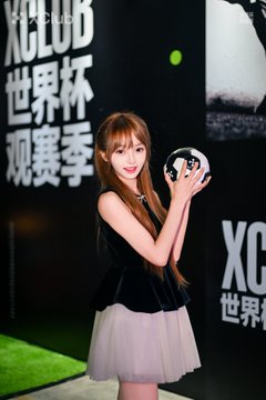 A woman in a black top and white tulle skirt holding a soccer ball at an XCLUB World Cup viewing event.