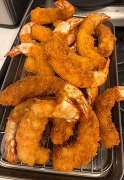 A close-up photo of freshly fried breaded shrimp arranged on a wire cooling rack over a baking tray.