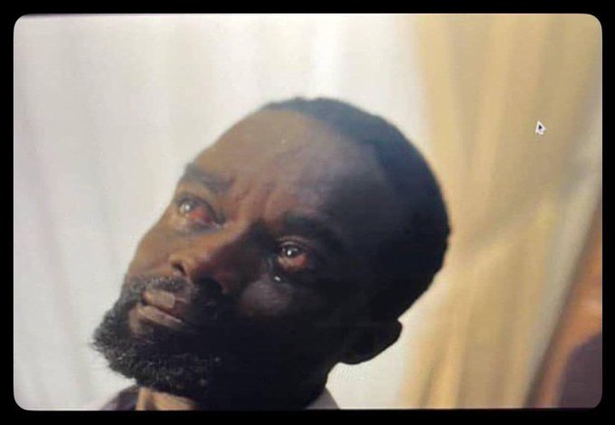 A close-up cinematic shot of a bearded Black man with a tear in his eye looking upward in a dimly lit room.