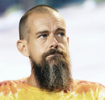 A portrait of a bearded man with a shaved head wearing a tie-dye orange shirt.