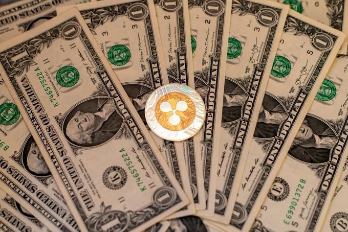 A fan of US one-dollar bills with a gold and silver XRP (Ripple) cryptocurrency coin resting on top in the center.