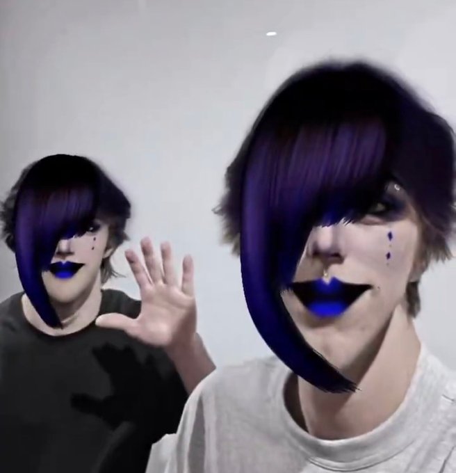 Two young creators with matching dramatic purple-streaked hair and dark gothic makeup, including black lipstick and small drawn-on tear drops beneath their eyes, pose against a plain white background, with one waving toward the camera. The scene reflects the accompanying post about NRG, capturing the high-energy, edgy aesthetic associated with the NRG (Nerium) subculture and dance trend that originated on Douyin.