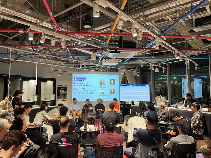 An audience sits at a 'BUILDER RIGHTS' panel discussing the invisible onchain experience, with a 'TOKYO GAME' sign visible in the background.