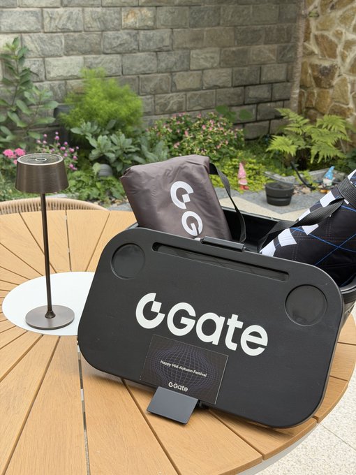 A GGate-branded black case sits on a wooden outdoor table alongside a matching bag and a lamp, with a stone wall and garden in the background.
