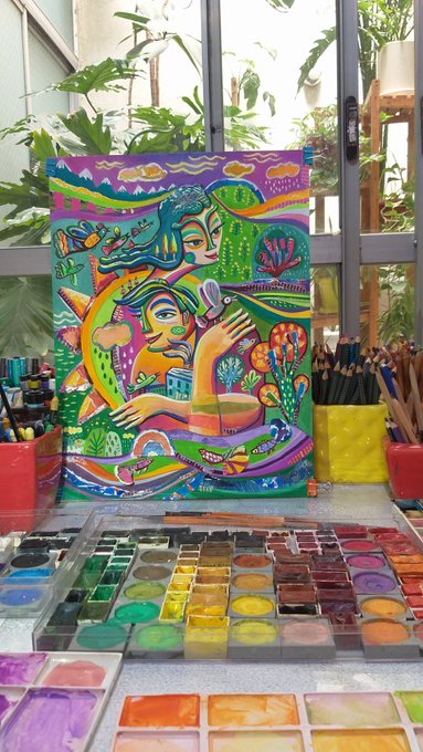 A vibrant, colorful painting featuring a woman with a crow and psychedelic nature elements, displayed in front of a window with potted plants and surrounded by watercolor palettes and colored pencils.