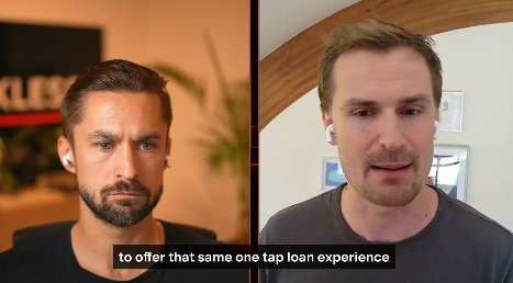 A split-screen video call shows two men; the left man has a beard and wears a black shirt, while the right man is clean-shaven in a grey shirt, with subtitles reading 'to offer that same one tap loan experience'.