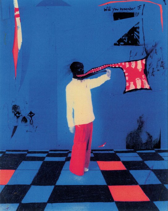 The image features a person standing on a checkered floor, wearing red pants and white shirt. They are holding up a piece of fabric that has a red design on it. The background includes a blue wall with graffiti art on it, as well as some other graffiti pieces scattered around the room. There is also a small clock visible in the scene. The image seems to be related to the post "GM summer waltz".