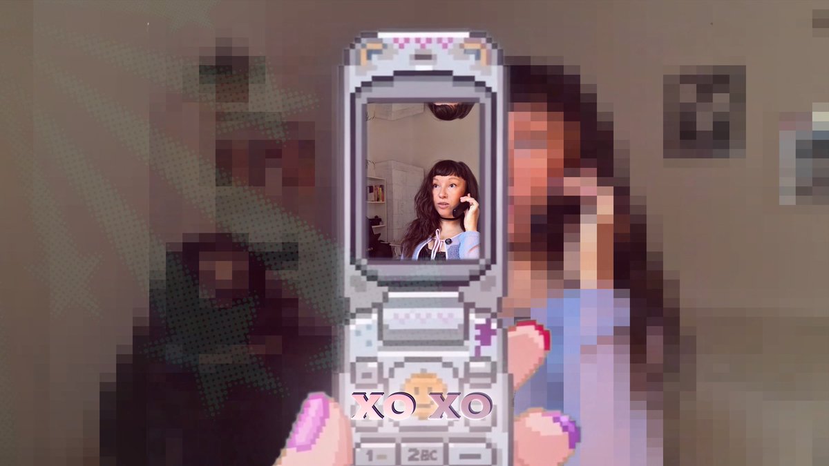 A hand holding a pixel-art style flip phone displaying a photo of a woman on the screen, with 'XOXO' text overlay and a blurred background.