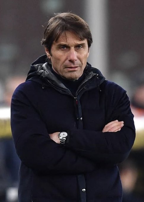 A man in a dark navy jacket with arms crossed, wearing a silver wristwatch.