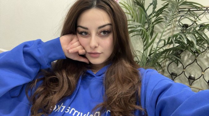 A young woman with long brown hair wearing a blue "Abercrombie & Fitch" hoodie takes a selfie, resting her cheek on her hand in a relaxed pose that matches her casual "felt cute, might take down later" caption.