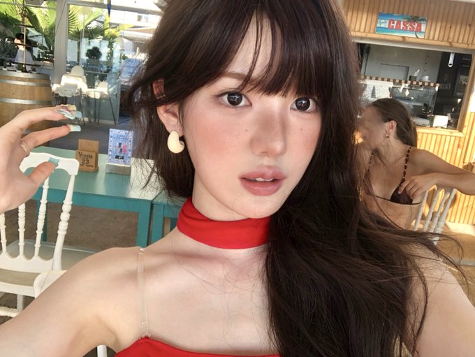 A young woman with long dark hair, wearing a red choker and matching top with cream-colored earrings, takes a close-up selfie at what appears to be an outdoor café or bar, with a "CHISSI" sign visible in the background. The hashtags #KiiiKiii, #키키, #SUI, and #수이 suggest this is a photo featuring Sui, a member of the K-pop group KiiiKiii.