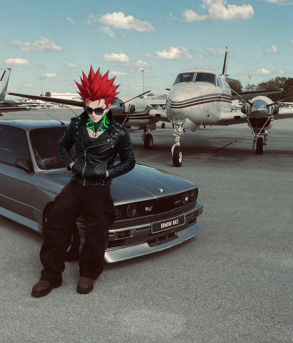 An anime-style character with spiky red hair and sunglasses leaning against a silver BMW M3 with a small airplane in the background on a tarmac.