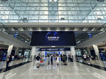 An airport terminal interior featuring a large digital advertisement displaying 'Goata.AI - Make bullish for AI' above travelers.