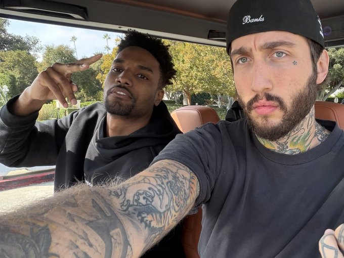 Two men take a selfie in a car, with the man on the right wearing a black "Banks" beanie and sporting visible neck and arm tattoos. The image accompanies a promotional post from streamer fazebanks announcing a live stream where he will be gifting money to viewers who reply with their Solana address, directing followers to watch on twitch.tv/fazebanks.
