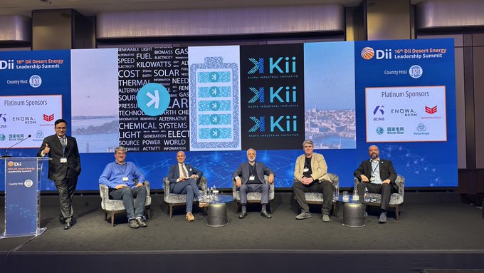 A panel of six men sits on a stage at the '15th DII Desert Energy Leadership Summit' hosted by Country Host, with sponsor logos including Kii and ENOWA displayed on large screens behind.