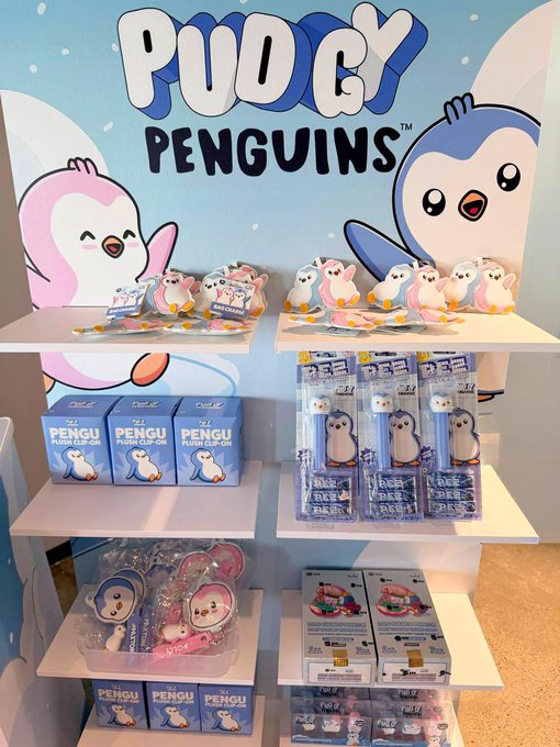 Retail display shelf featuring Pudgy Penguins merchandise, including plush clip-on toys and PEPE branded products.