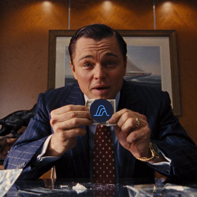 A man in a pinstripe suit and red tie holds up a card featuring a blue A-shaped logo, resembling a scene from The Wolf of Wall Street.