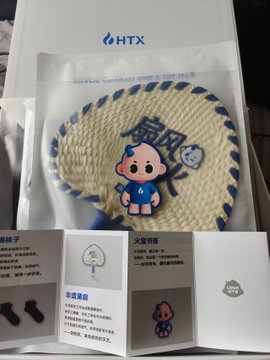 The image features a white box with a blue and yellow cartoon character on it, along with some instructions written in Chinese. The box contains a fan and a sticker that says "@HTX_Molly" or "@Ceee333". There is also an instruction manual for assembling the fan inside the box.