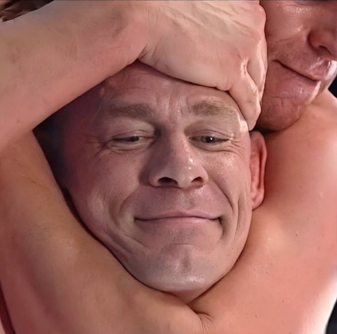 Close-up of a man's face appearing emotional or tearful while being held in what looks like a wrestling or grappling hold, with another person's face partially visible pressed against him.