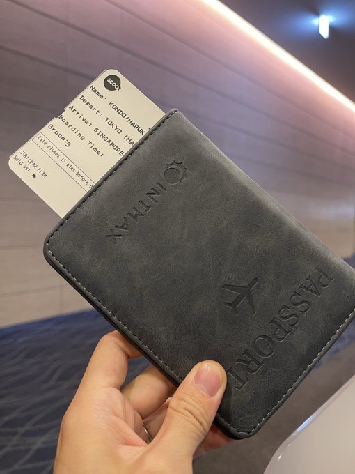 A hand holds up a dark gray "INTMAX PASSPORT" leather case containing a Singapore boarding pass issued to KONDO HARUKI, showing the post celebrating that this traveler is using an INTMAX passport case on their trip to Singapore.