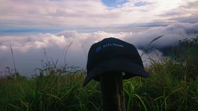 The image features a black baseball cap sitting on top of a wooden pole, which is located at the top left corner of the frame. The background includes a sky filled with clouds and grassy areas, giving off a serene atmosphere. The caption "Without Solana and BNB maybe I wouldn't have this space... is there anything the same?" suggests that someone might be comparing the hat to two popular companies: Solana and BNB (Bank of Nova Scotia).