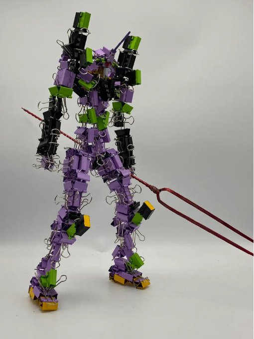 A handmade sculpture of a mecha robot figure constructed from purple, green, and black binder clips, holding a red pitchfork-like weapon.