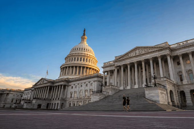 The U.S. Capitol Building stands prominently against a clear blue sky at dusk, with two figures walking on the steps below. The image accompanies news that Galaxy Digital has reduced its forecast for the Digital Asset Market Clarity Act passing in 2026 to just 10%, highlighting the legislative challenges facing crypto regulation in Washington.