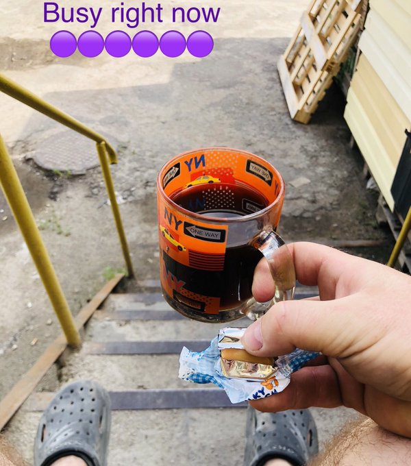 A first-person view of a hand holding a small snack and a glass mug of dark liquid with an 'NY ONE WAY' design, with text reading 'Busy right now' and several purple circles.