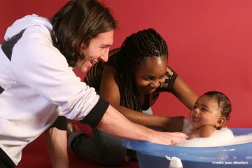 A woman bathes a smiling child in a blue tub while another woman leans in with a playful expression against a red backdrop, with a "Credit: Jean Monbet" watermark visible. The tender family moment visually echoes the post's theme of ritualistic cycles and meaningful numbers, as the date 7/19/2026 completes a 366-day arc from XRP's $3.66 peak tied to the Genius Act.