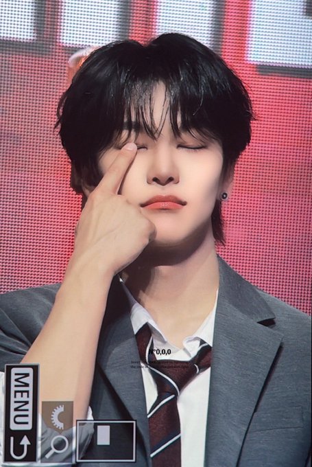 The image features a young man with short hair wearing a suit, tie, and white shirt. He has his hand up to his face, making a funny or cheeky gesture as if he's making a silly face for the camera. The background of the photo is red, which contrasts with the man's attire and adds visual interest to the image. There are also some text elements in the picture that read "260620 님 입꼬리어디까지 내려갈거에요⇩⇩⇩ #허씬롱 #씬롱 #XINLONG #ALPHADRIVEONE #ALD1". These elements contribute to the overall composition and context of the image, making it a visually engaging piece.