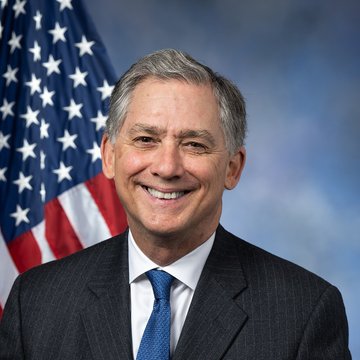 A smiling older man with gray hair, wearing a dark suit and blue tie, poses for an official portrait with an American flag in the background. The image appears to be an official congressional photo, likely of Rep. French Hill, who is mentioned in the accompanying post about the CLARITY Act.
