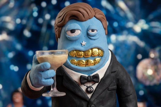 A clay figurine of a blue-faced character in a tuxedo with gold teeth holding a cocktail glass, set against a sparkly blue background.