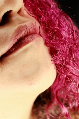 A close-up photograph focuses on the lower half of a person's face, showing pink lips and bright pink curly hair.