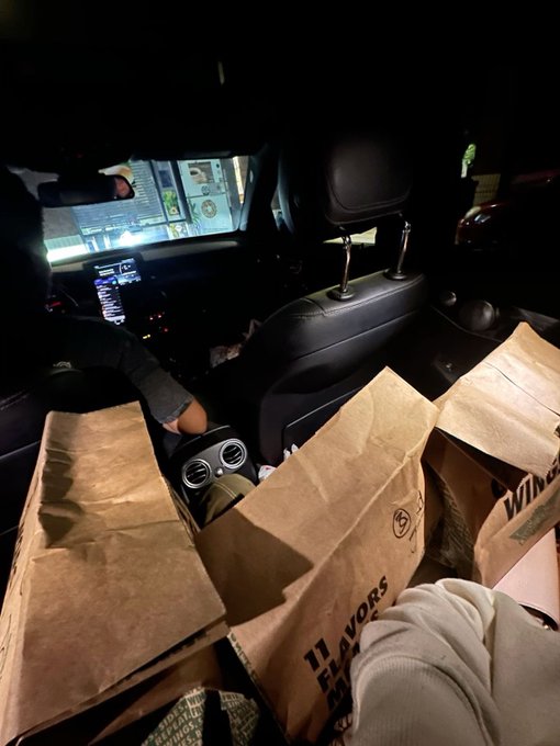 Interior view of a vehicle at night with brown paper shopping bags placed on the passenger seat and footwell.
