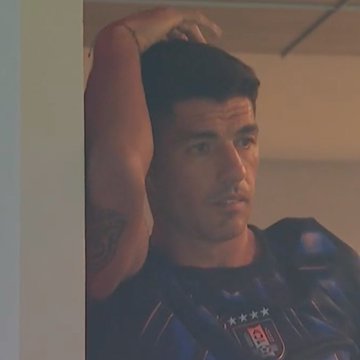 A young man wearing a black shirt with a blue design underneath is leaning against a wall looking downward while scratching his head or resting his elbow. The photo also appears to be of a man sitting at a table, possibly enjoying some refreshments or food. This image seems unrelated to the current event being discussed in the context provided by the post about Cape Verde's World Cup victory.