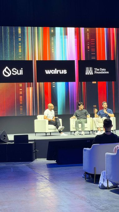 Photo of a panel discussion at a conference with three speakers seated on stage in front of banners for Sui, Walrus, and The Data Foundation.
