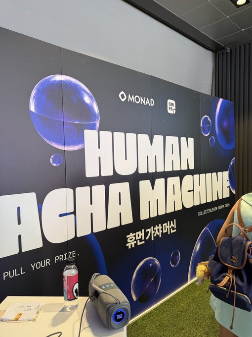 A promotional booth display for 'HUMAN ACHA MACHINE' collection by MONAD and ORI PAL, featuring bubble graphics and the text 'PULL YOUR PRIZE' with prizes on display.