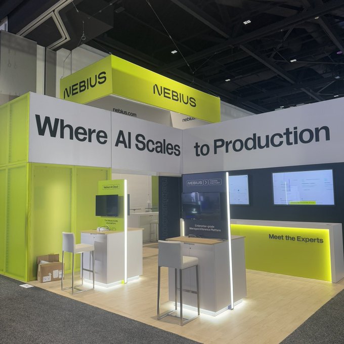 The image shows an exhibit booth for a company named "Nebius", which has a green background with white text, including the words "Where AI Scales to Production" written above their name. The booth also features two chairs positioned near each other in front of a TV screen displaying the NASDAQ 100 index. A sign on the booth reads "When the stock market opens tomorrow nebius $NBIS will be a member of the NASDAQ 100".