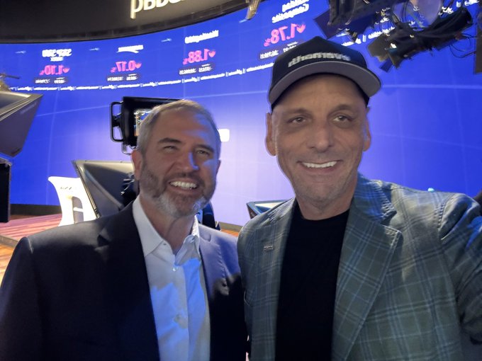 Two men smile and pose together in a TV studio setting with blue screens in the background.
